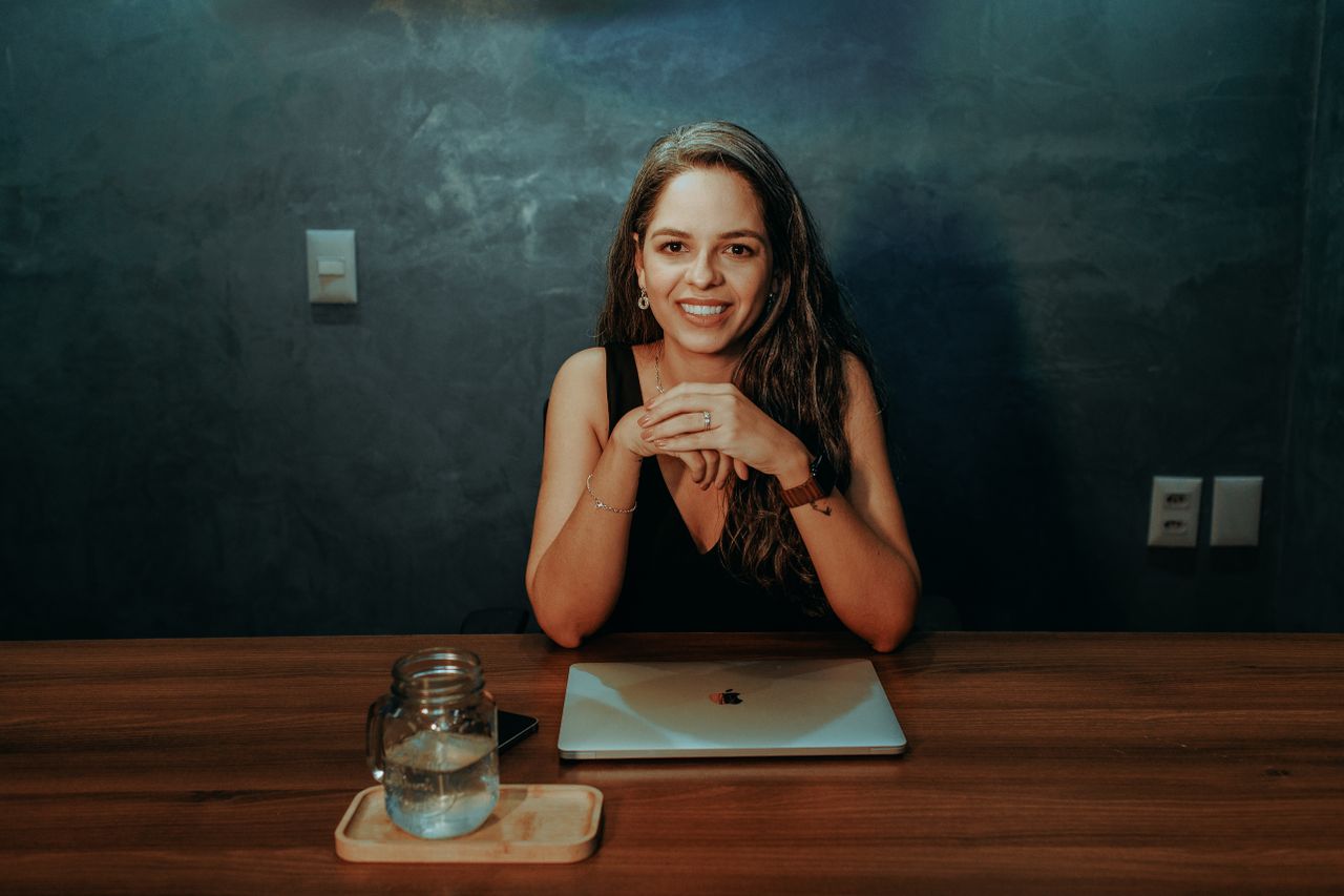 Services A brunette woman sitting at a desk with a laptop, smiling in an elegant office setting.